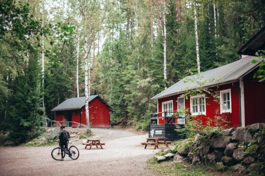 Exterior of a cabin in the woods and a man on a bike