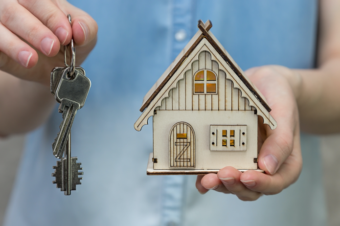 Close up of hands holding a miniature house and a set of keys
