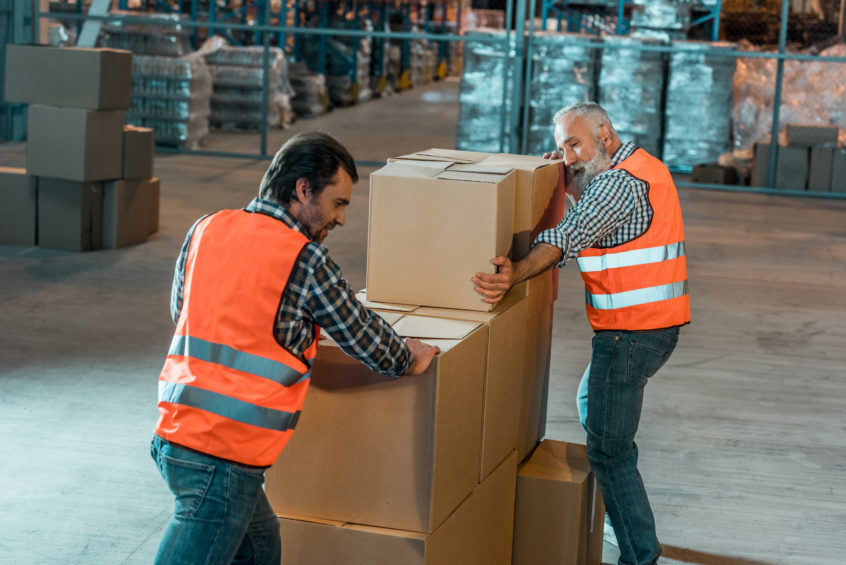 Warehouse workers in vests moving boxes in storehouse